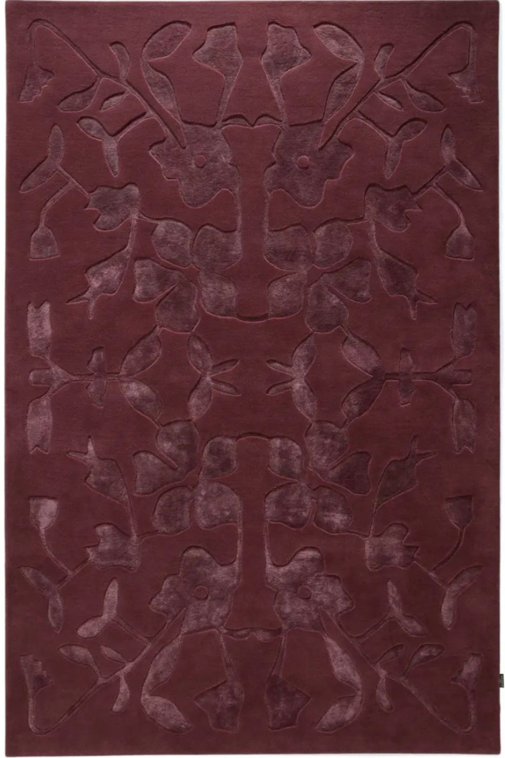 A rectangular area rug in a deep burgundy color, featuring a raised, symmetrical abstract floral or vine pattern across the surface.