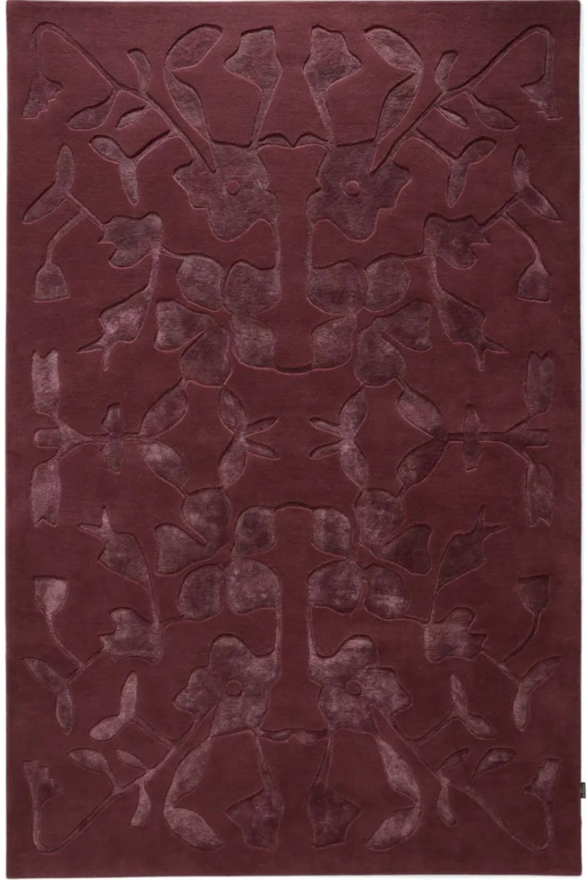 A rectangular area rug in a deep burgundy color, featuring a raised, symmetrical abstract floral or vine pattern across the surface.