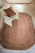 Brown oval rug with a white chair and brown pillow on a wooden floor.