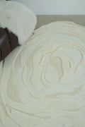 Close-up of a textured beige rug with a brown chair and white fur rug in the background.