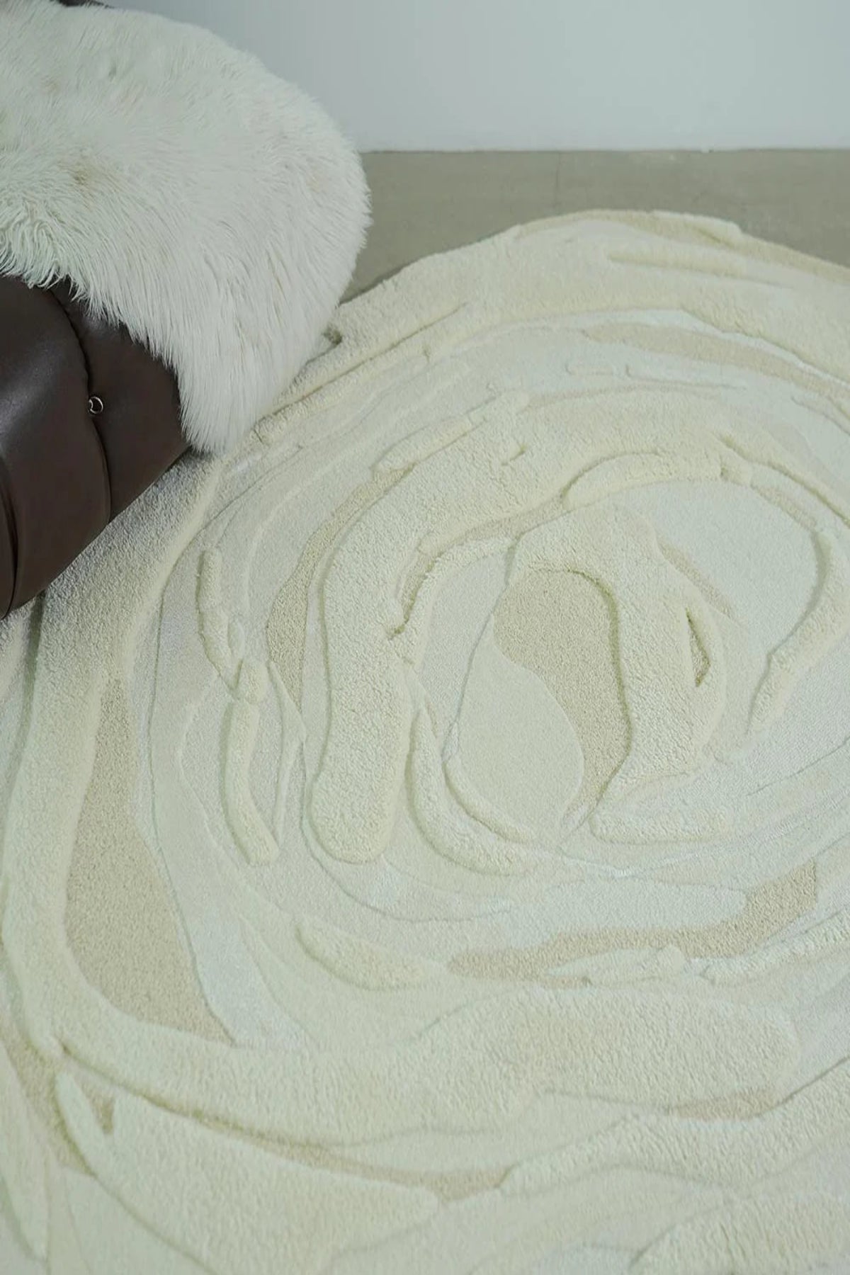 Close-up of a textured beige rug with a brown chair and white fur rug in the background.