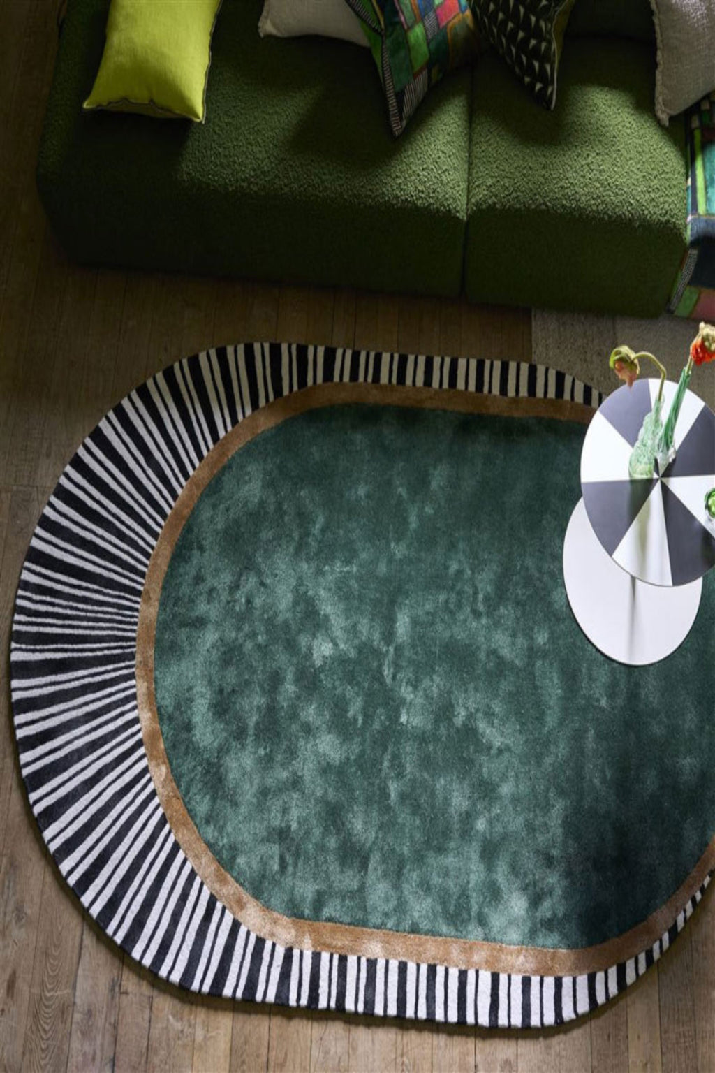 Green oval rug with black and white striped border in a living room setting.