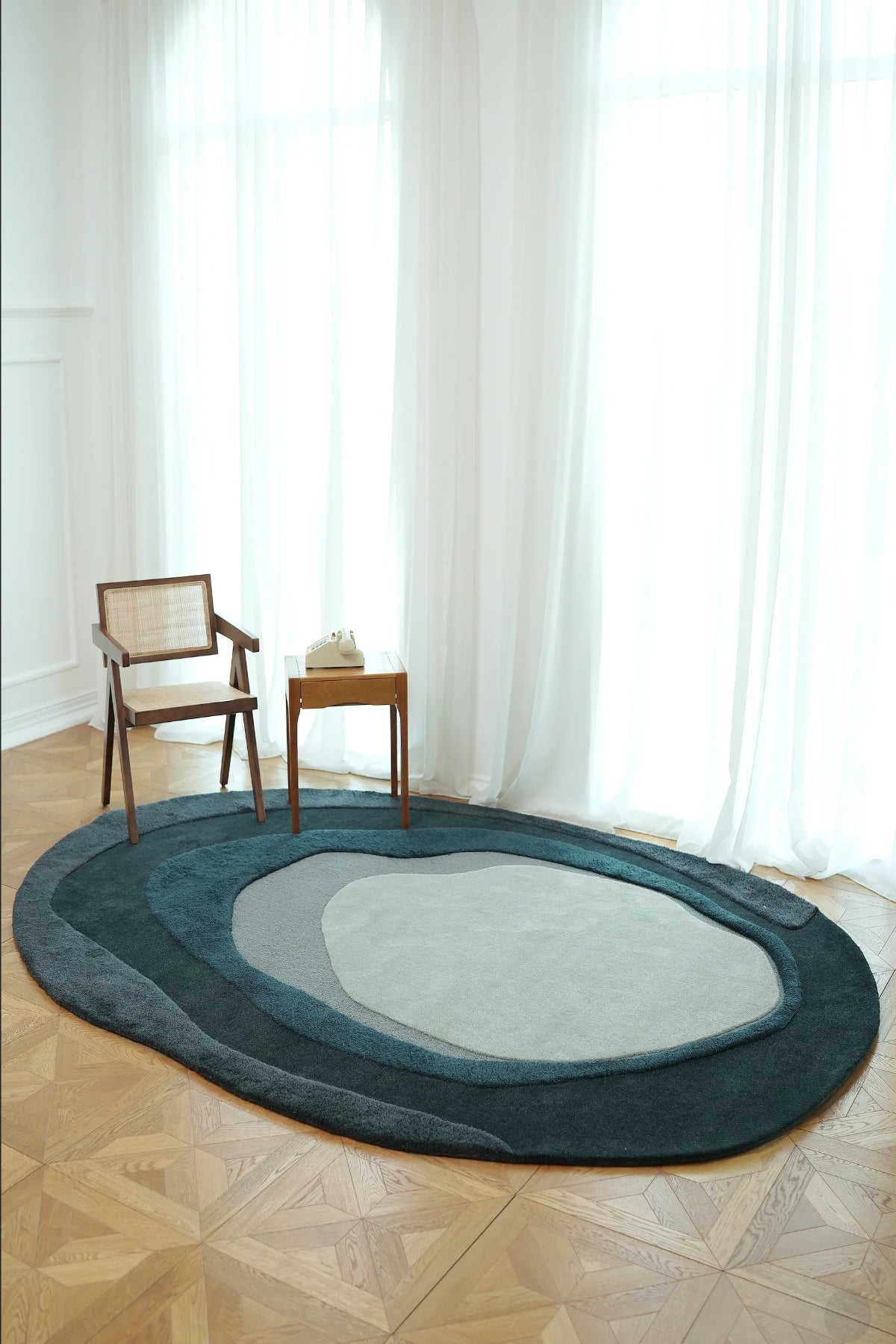 Oval-shaped rug on a wooden floor with a chair and small table in front of large windows.