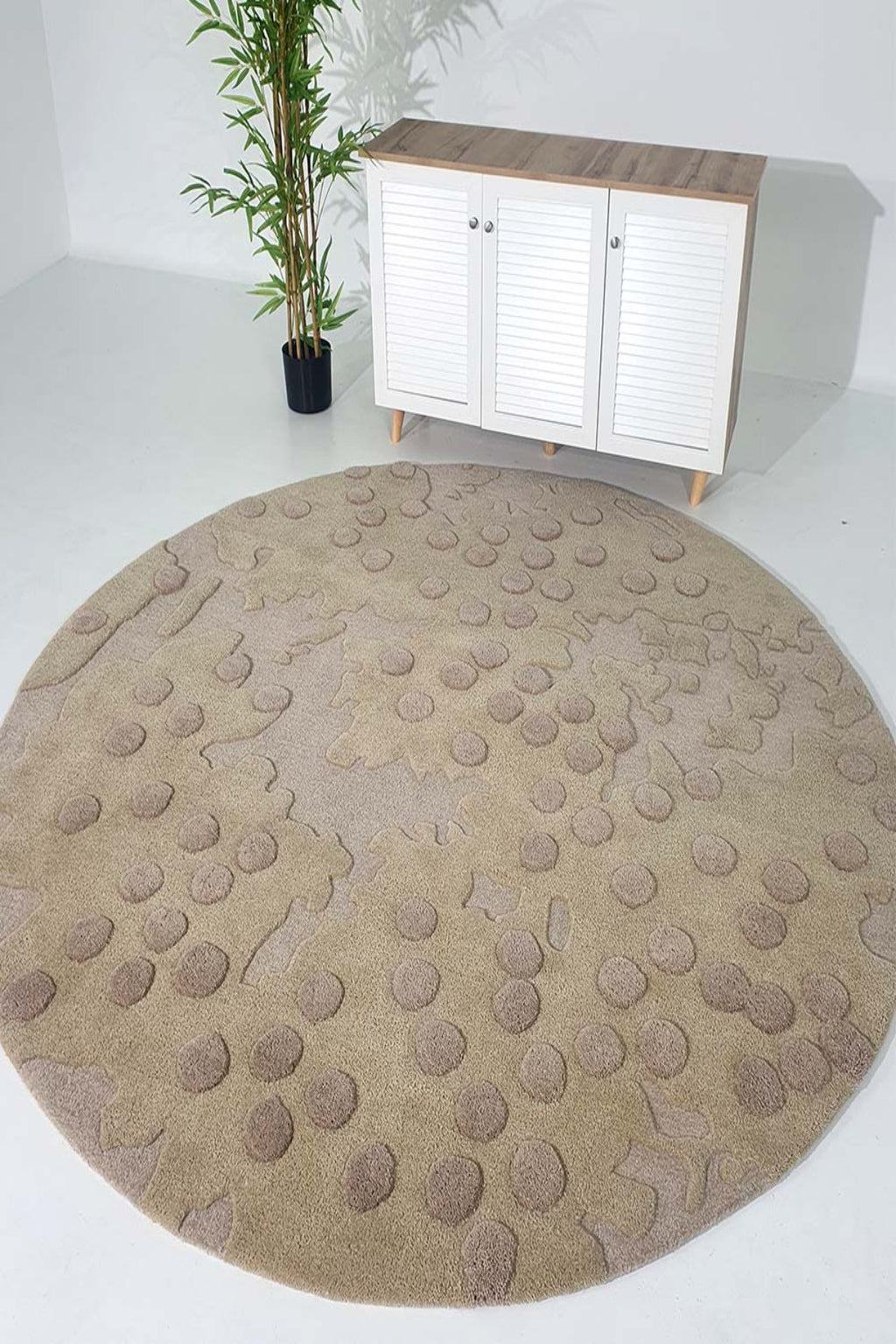 Round beige rug with textured pattern in a room with a white cabinet and plant.