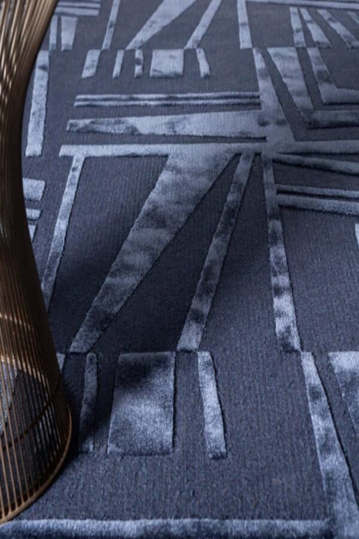 Close-up of a dark blue geometric patterned rug with a woven chair corner.