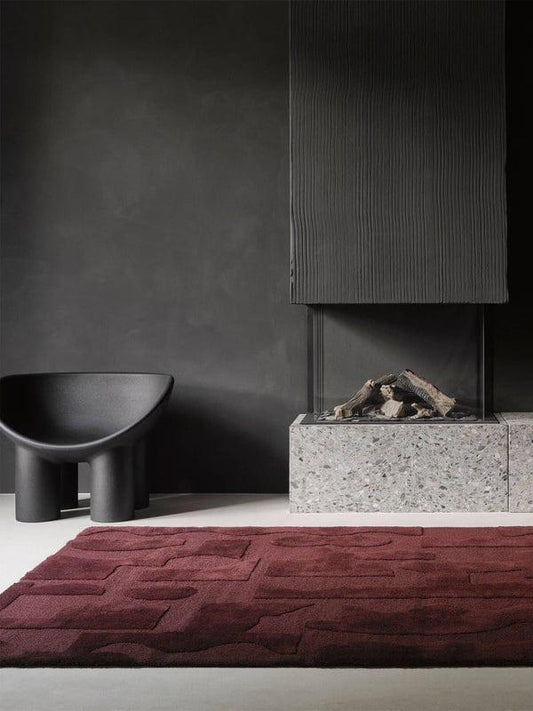 Modern interior with a dark gray wall, black chair, and red textured rug.
