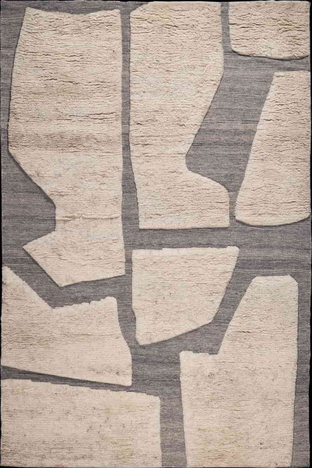 Abstract area rug with irregular beige stone-like shapes on a textured gray background.