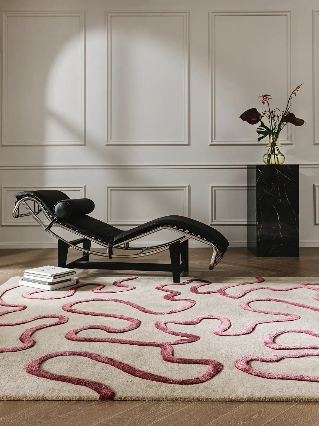 Modern chaise lounge against a wall with a decorative pink rug on a wooden floor.