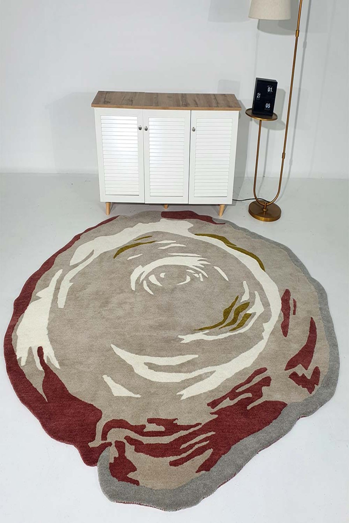 Round area rug with artistic design on a white floor, featuring a cabinet and lamp in the background.